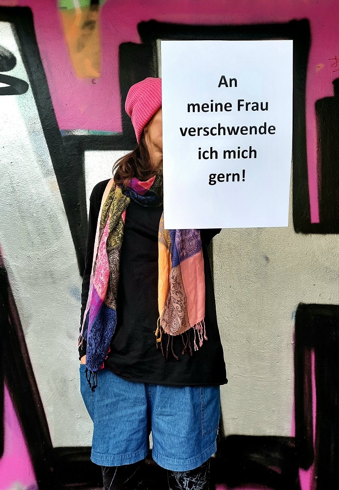 Ein Foto von einer jungen Frau, die einen beschrifteten Zettel vor sich hält.