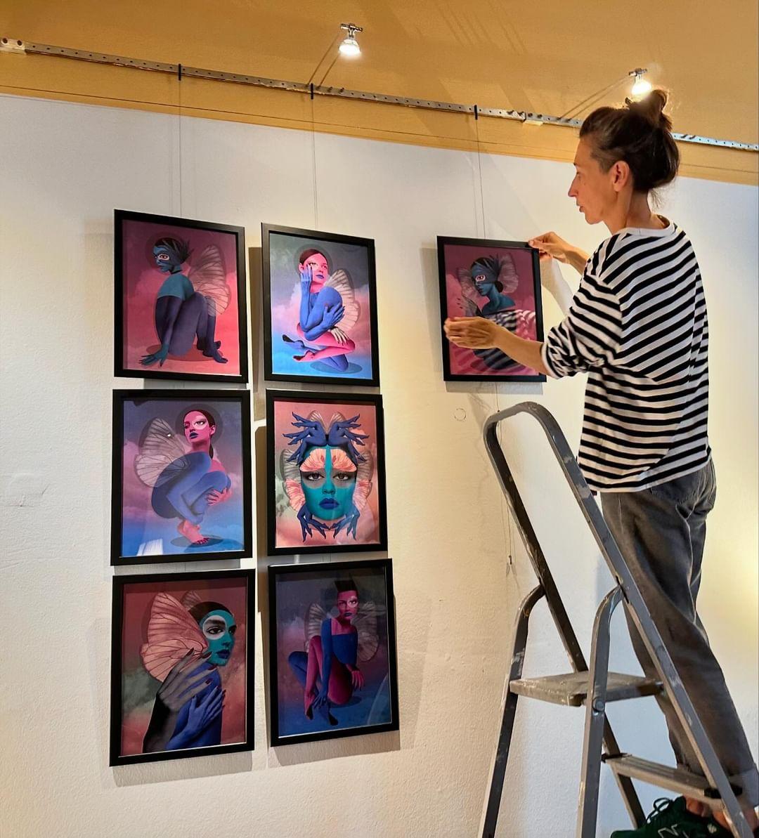 Ein foto von einer Frau, die auf einer Leiter steht und ein Bild an die Wand hängt. 