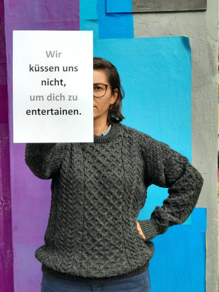 Ein Foto von einer jungen Frau mit Brille, die einen beschrifteten Zettel vor sich hält.